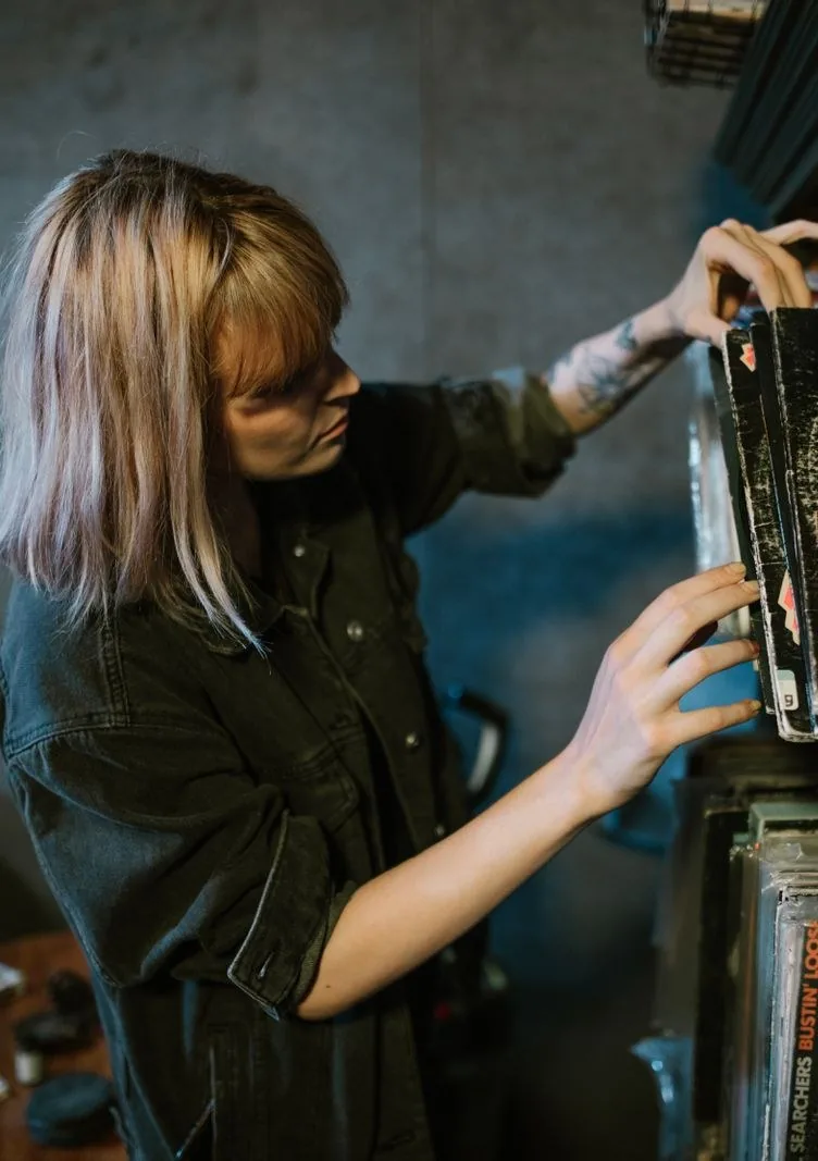A person carefully sliding a vinyl record out of a wooden shelf to inspect it