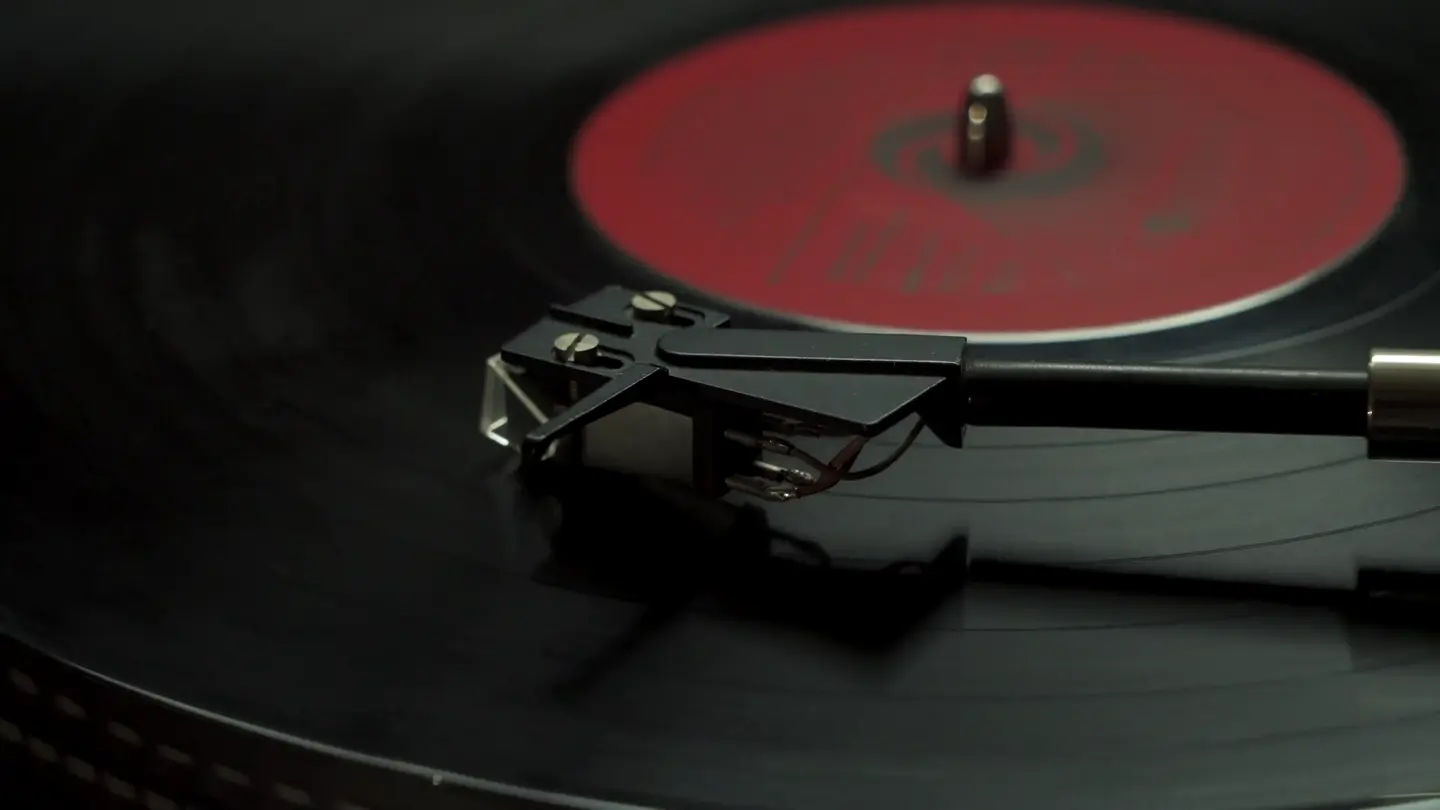 Close-up of a turntable needle resting on a vinyl record with a red label